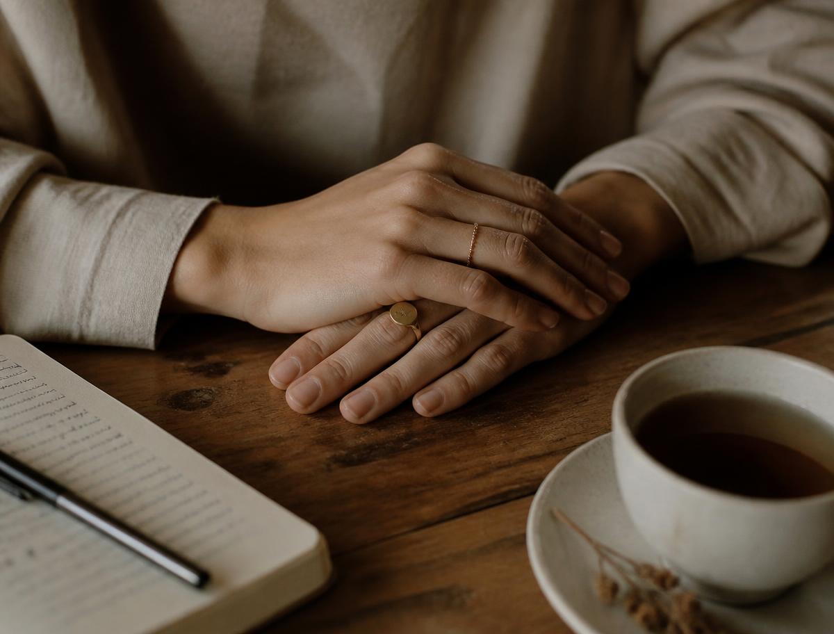 Hands resting calmly on a table beside a notebook and tea