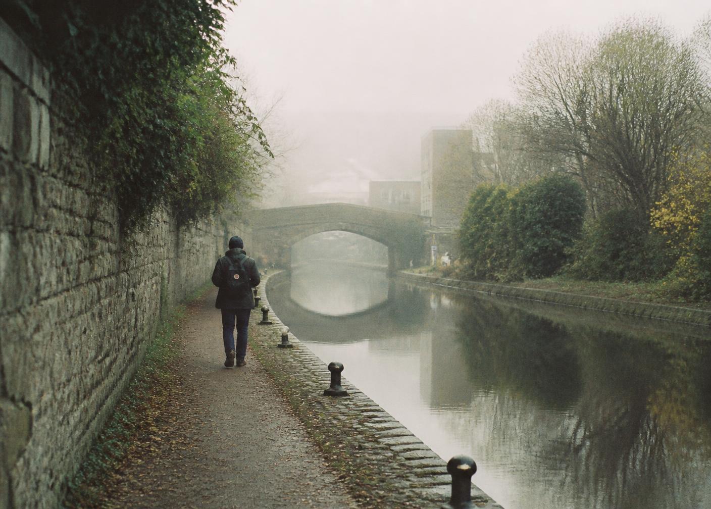 A person walking alone along a quiet Dublin canal in morning mist